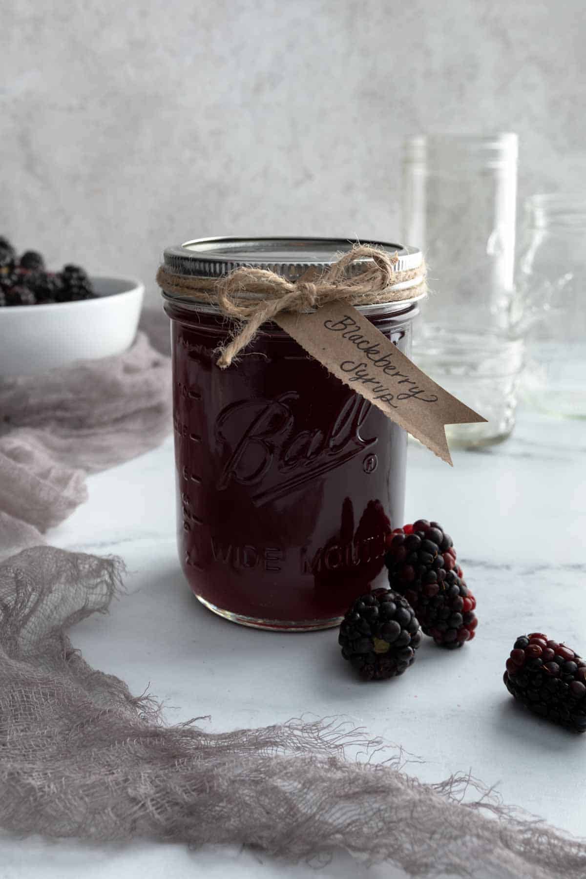 A mason jar full of blackberry syrup with a twine bow and handwritten label