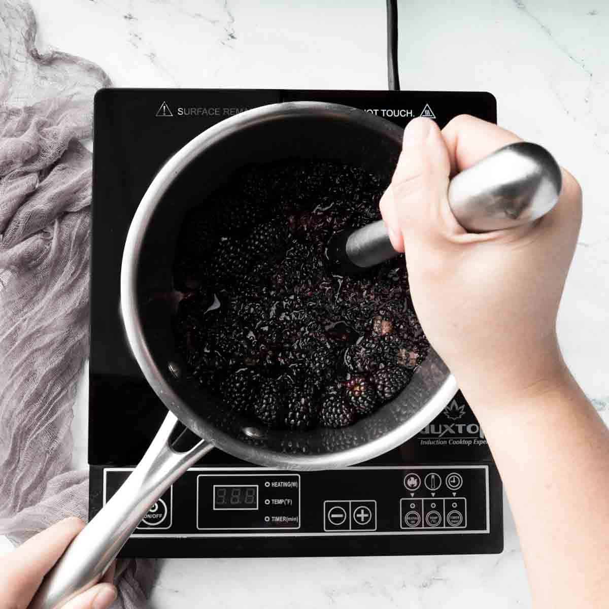 Muddling blackberries in a stainless steel pot