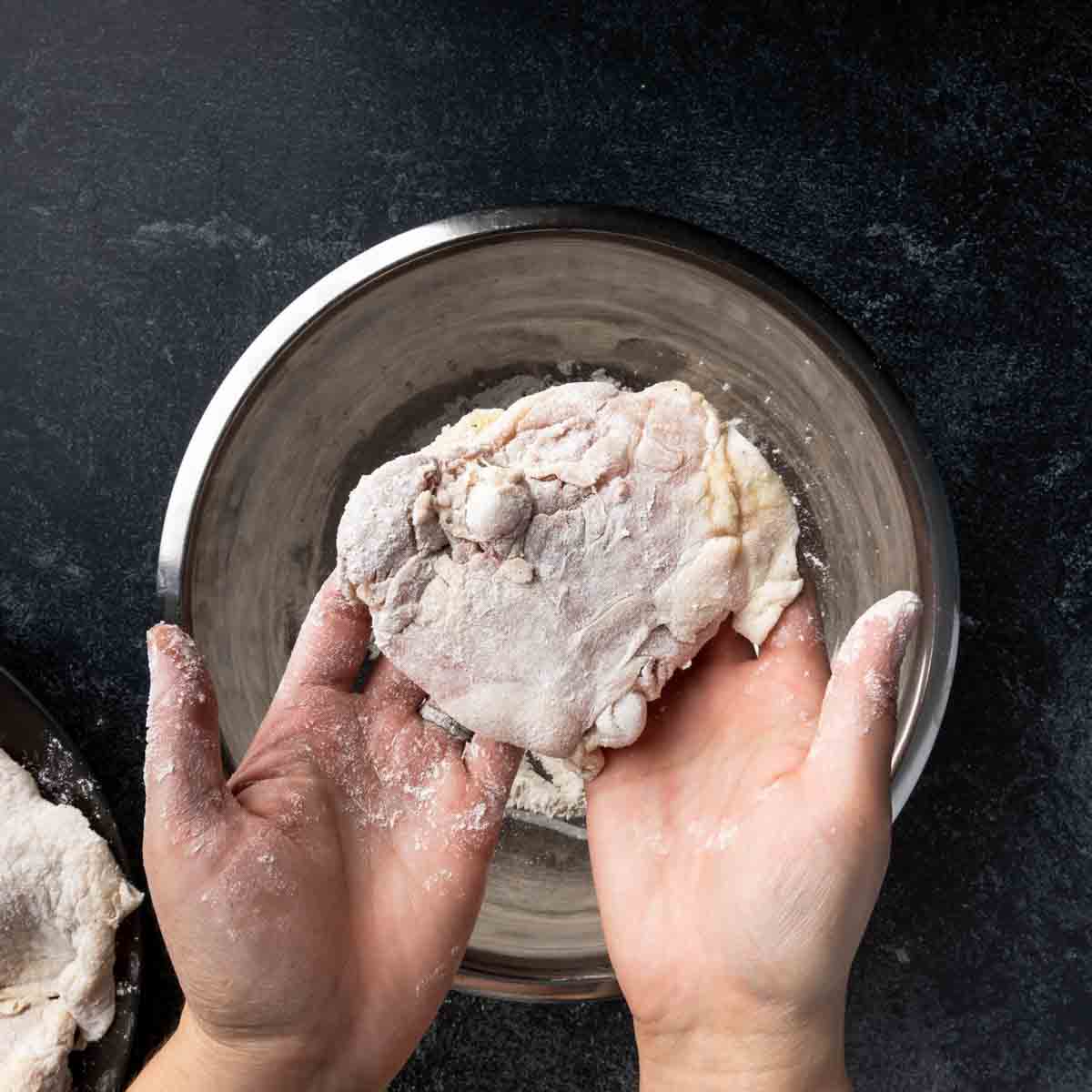 Dredging a bone in skin on chicken thigh in seasoned flour