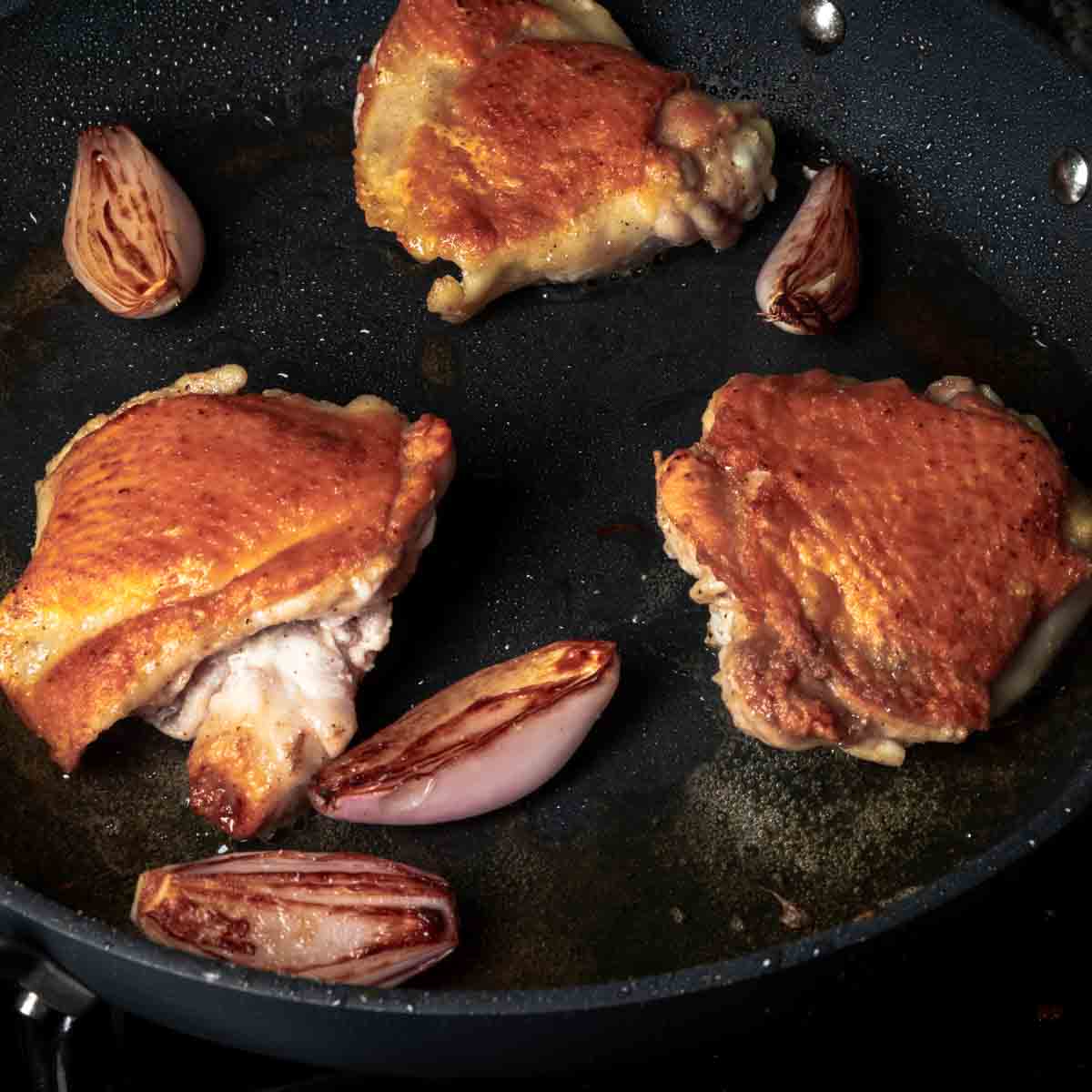 Golden brown chicken thighs and shallots in a frying pan