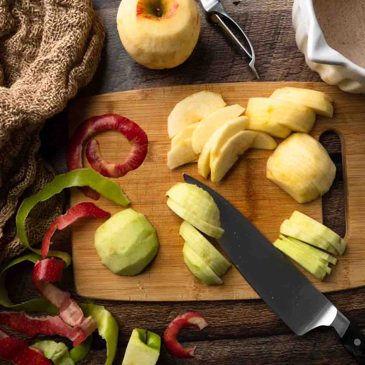 A cutting board filled with sliced apples, apple peels and a knife