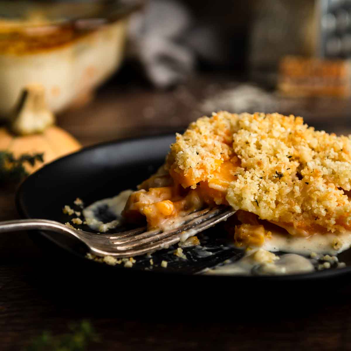 A fork on a plate with a big serving of cheesy butternut squash casserole