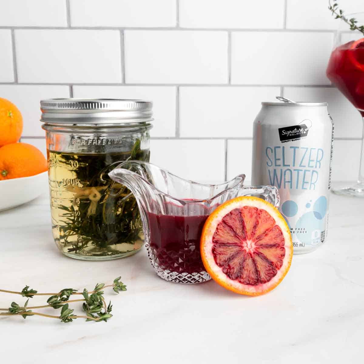 A jar of thyme simple syrup, freshly squeezed blood orange juice and a can of seltzer. 