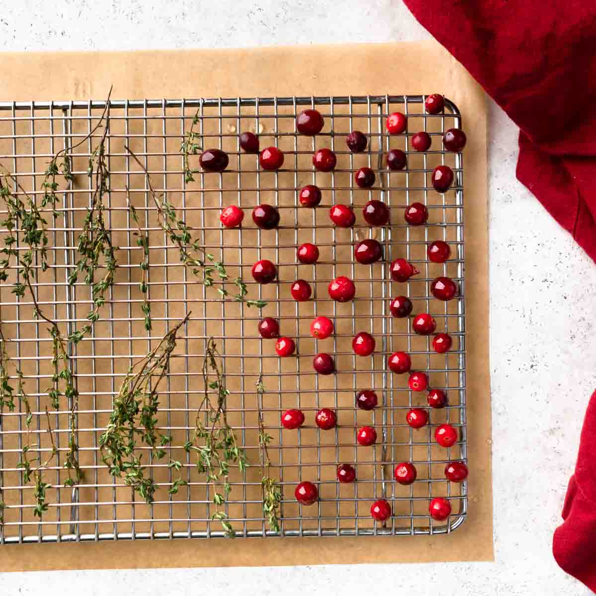 Simple syrup glazed cranberries and thyme sprigs drying on a wire rack.