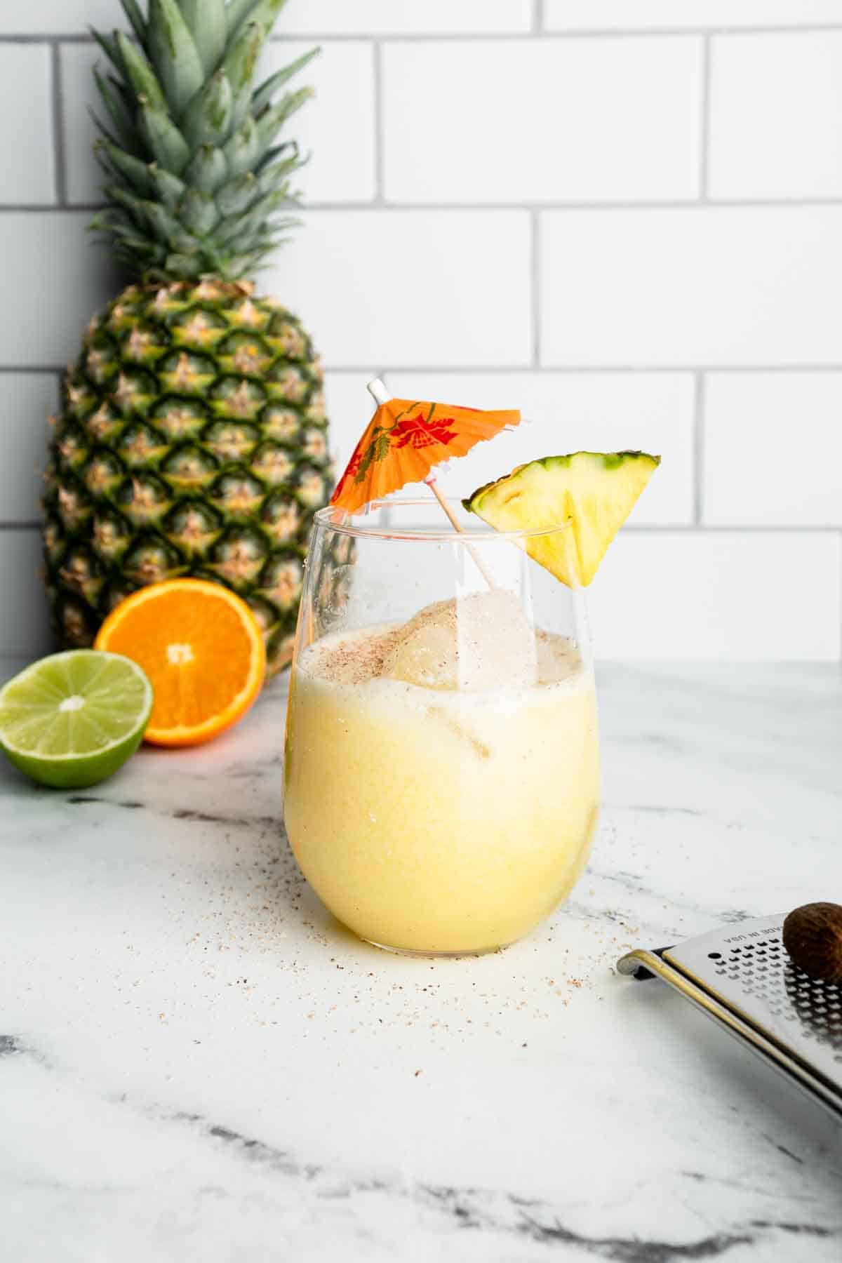 A coconut and pineapple mocktail garnished with fresh pineapple and a cocktail umbrella.