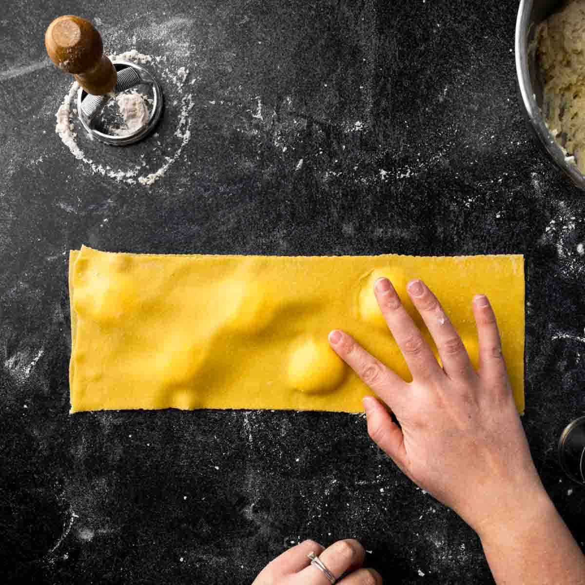 Sealing pasta dough around the ravioli filling with fingertips.