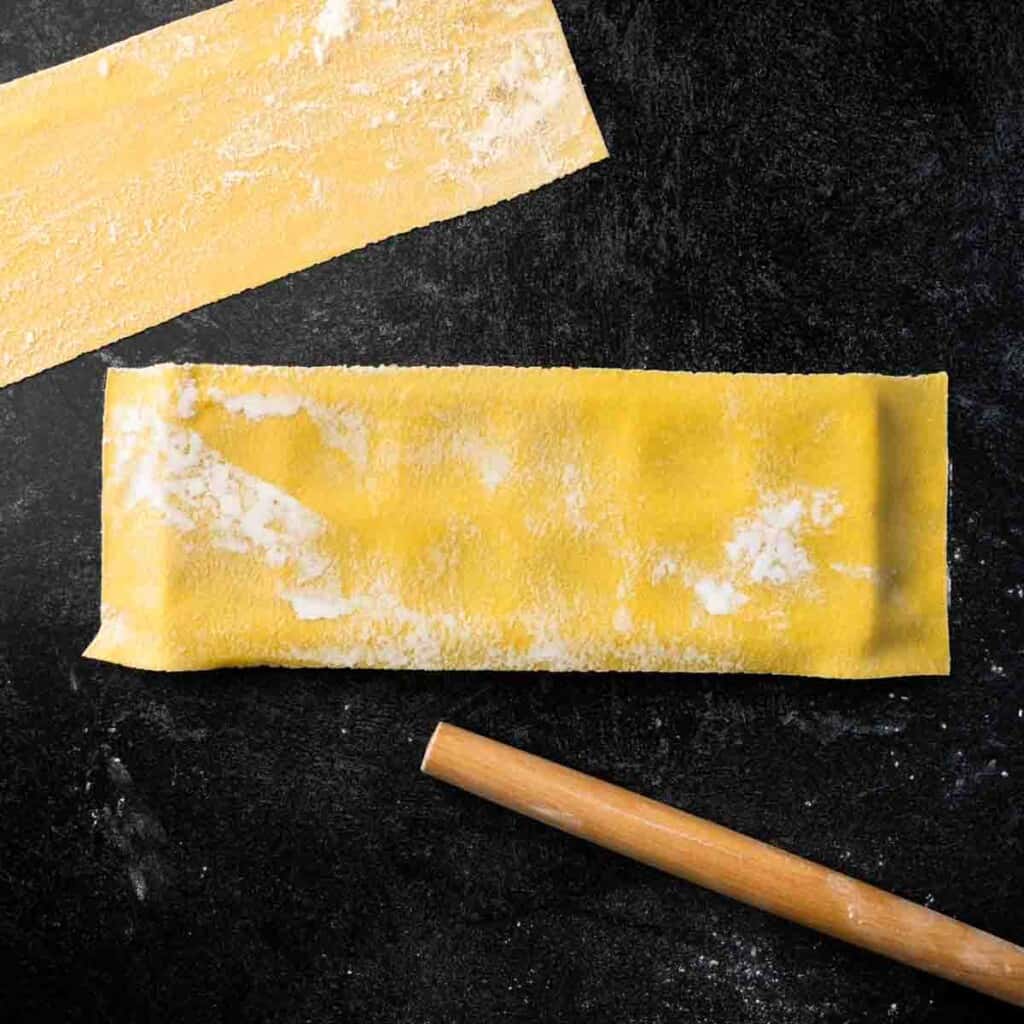 A sheet of floured pasta dough laying over a ravioli maker frame.