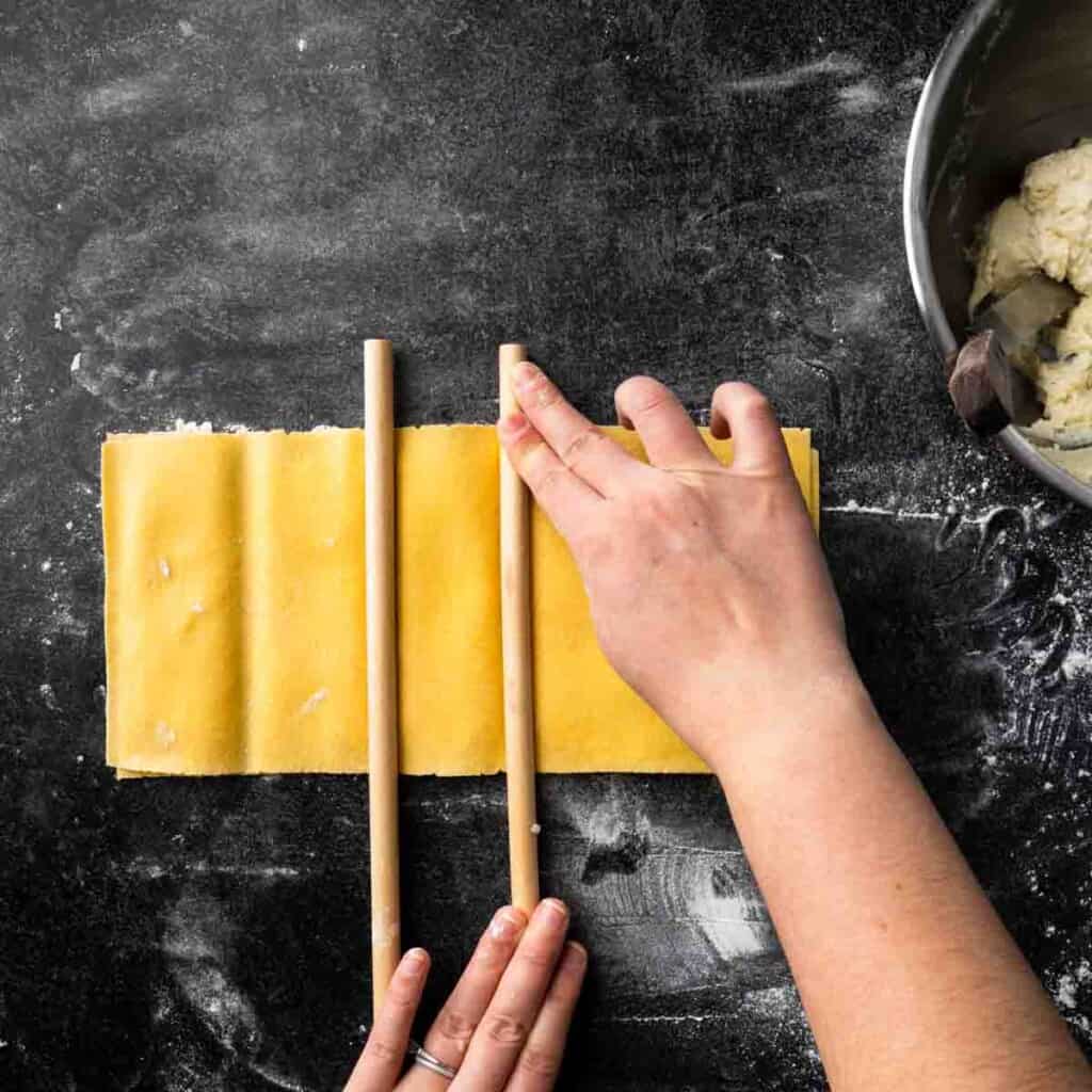 Pressing dowels into sheets of pasta sandwiched with ravioli filling. 