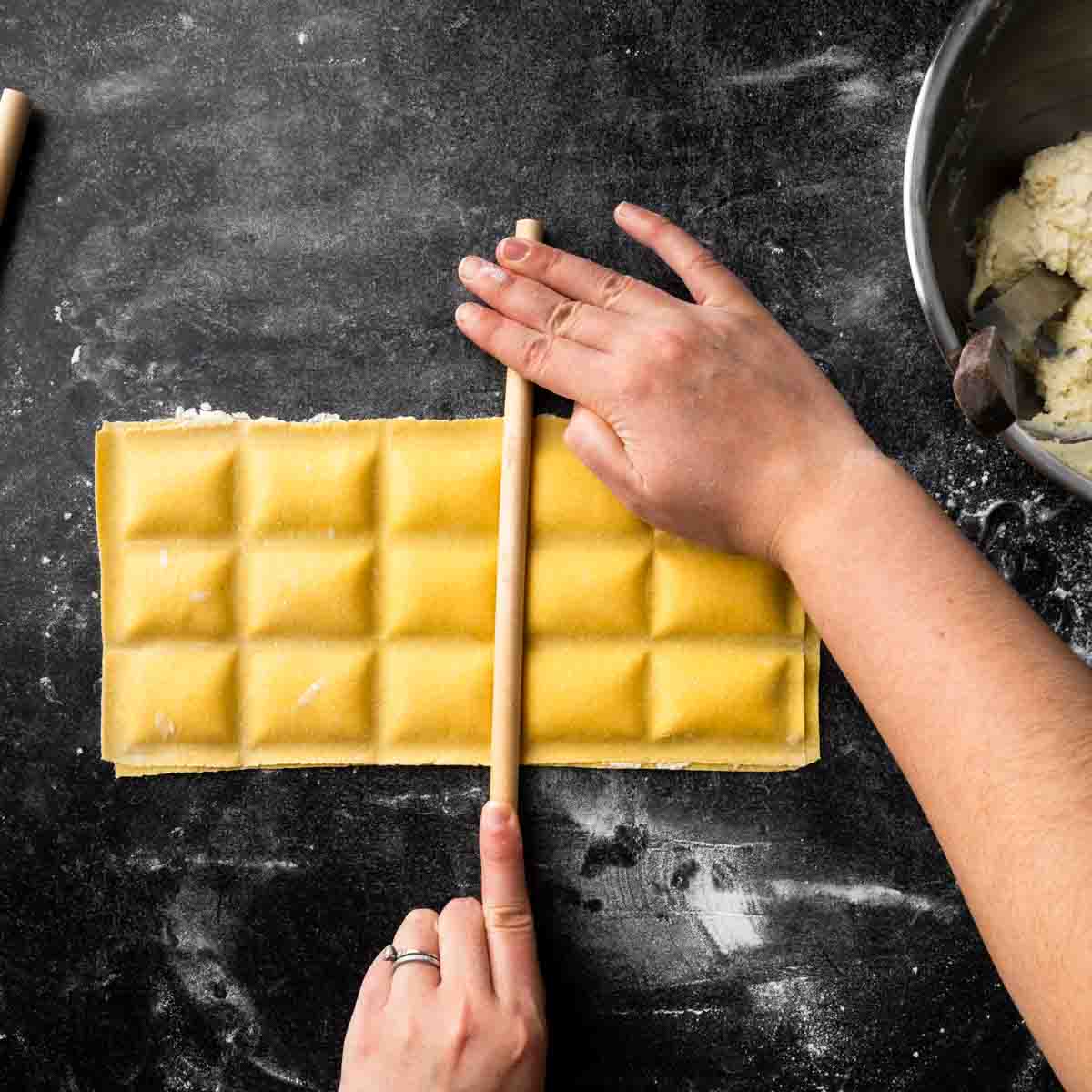 Firmly pressing a dowel into the ravioli to create an even shape and seal.