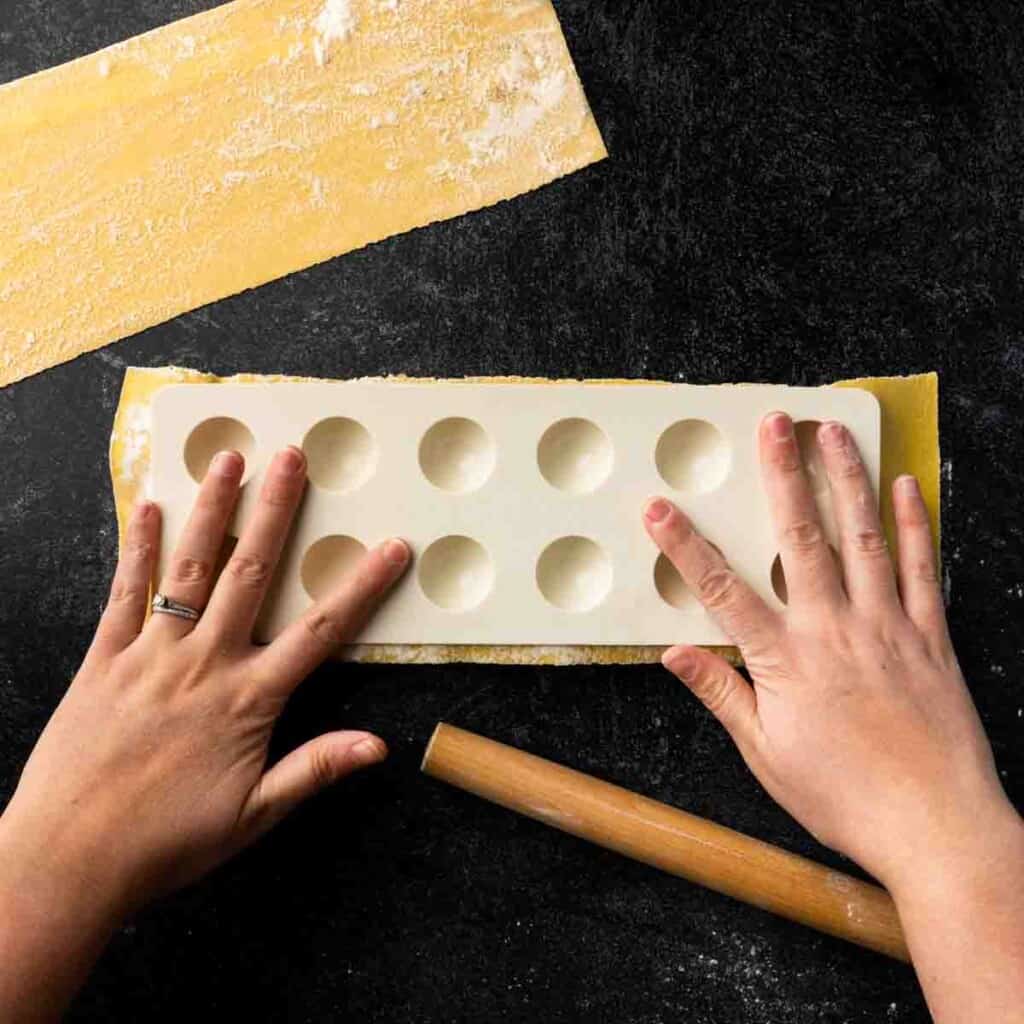 Hands pressing the plastic domed portion of a ravioli maker over the pasta dough.
