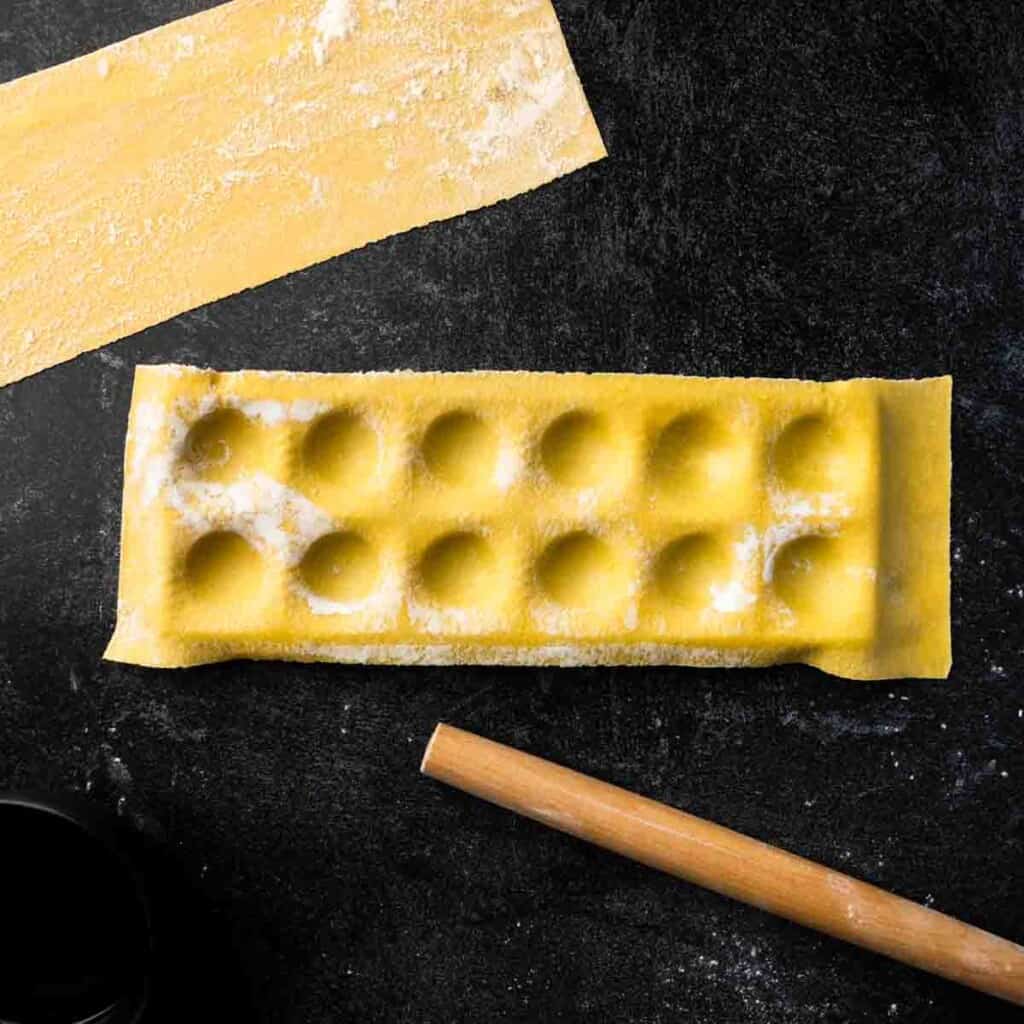 The indented pasta dough laying over the ravioli maker frame.