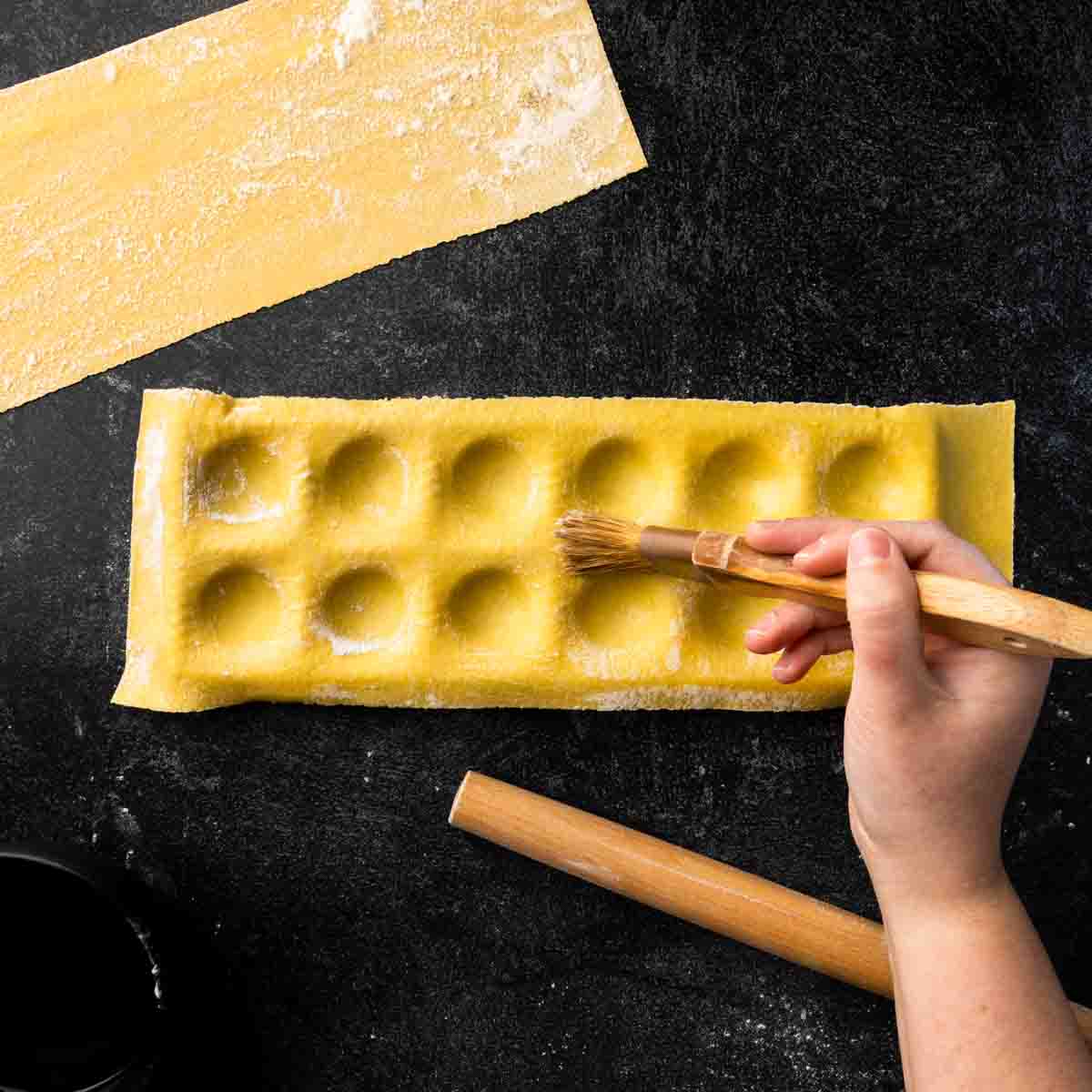 Brushing the edges of the ravioli indentations with a damp pastry brush.