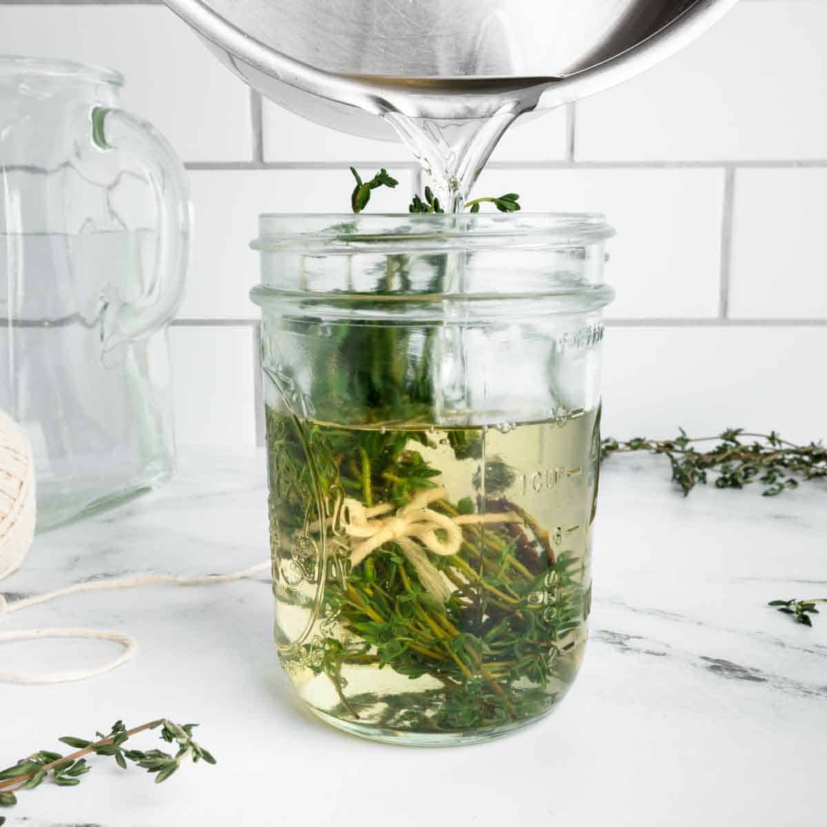 Pouring simple syrup into a jar with a bundle of blanched thyme.