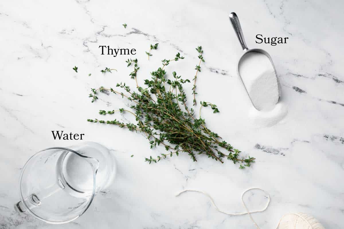 A pitcher of water, fresh thyme sprigs and a scoop of granulated sugar.