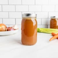 A jar of chicken feet bone broth and aromatic vegetables.