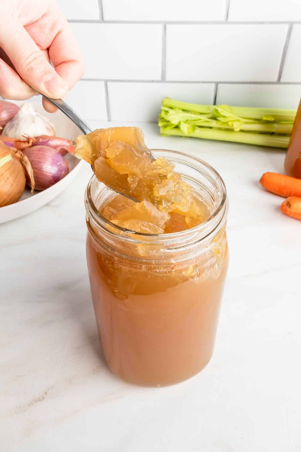 A spoon scooping a gelatinous chicken feet bone broth in a jar.