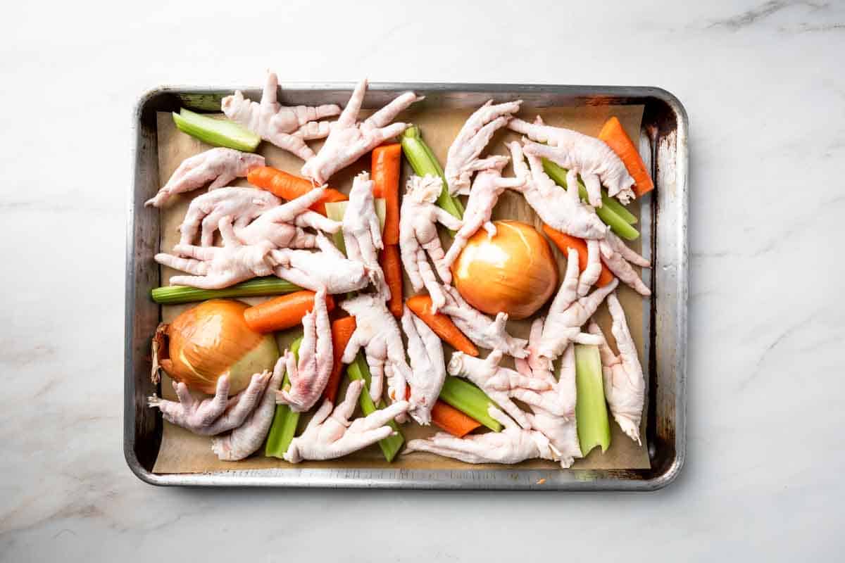 Raw chicken feet and mire poix on a sheet pan.