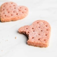 A heart shaped strawberry shortbread cookie with a bite missing.