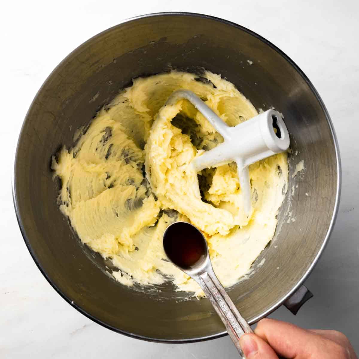 Adding vanilla to a stand mixer with creamed butter and sugar.