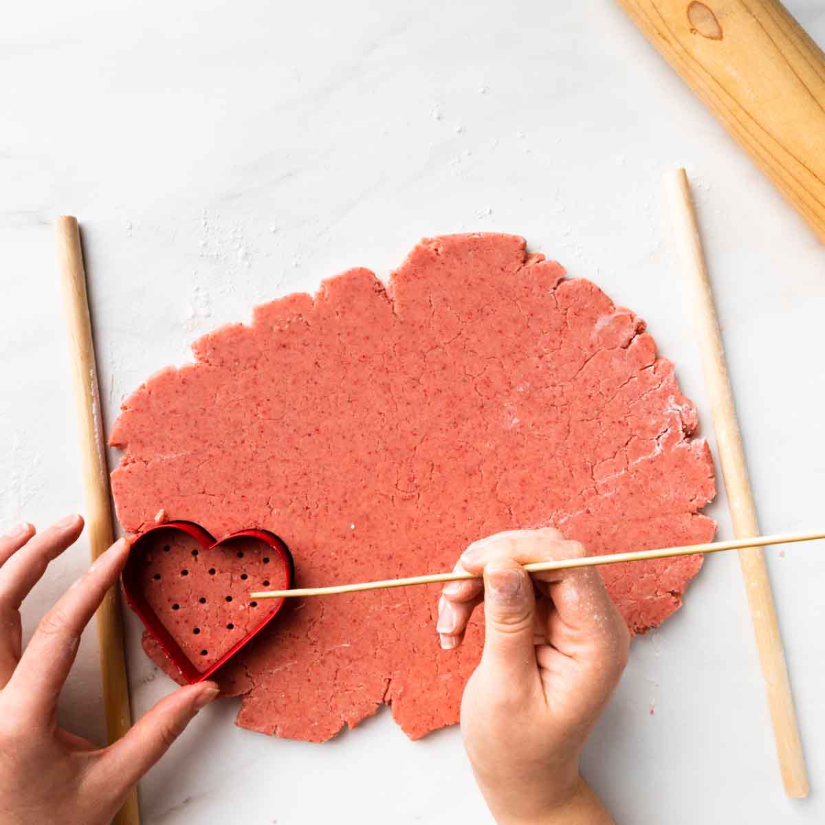Using a skewer to dimple and decorate a heart shaped cookie.
