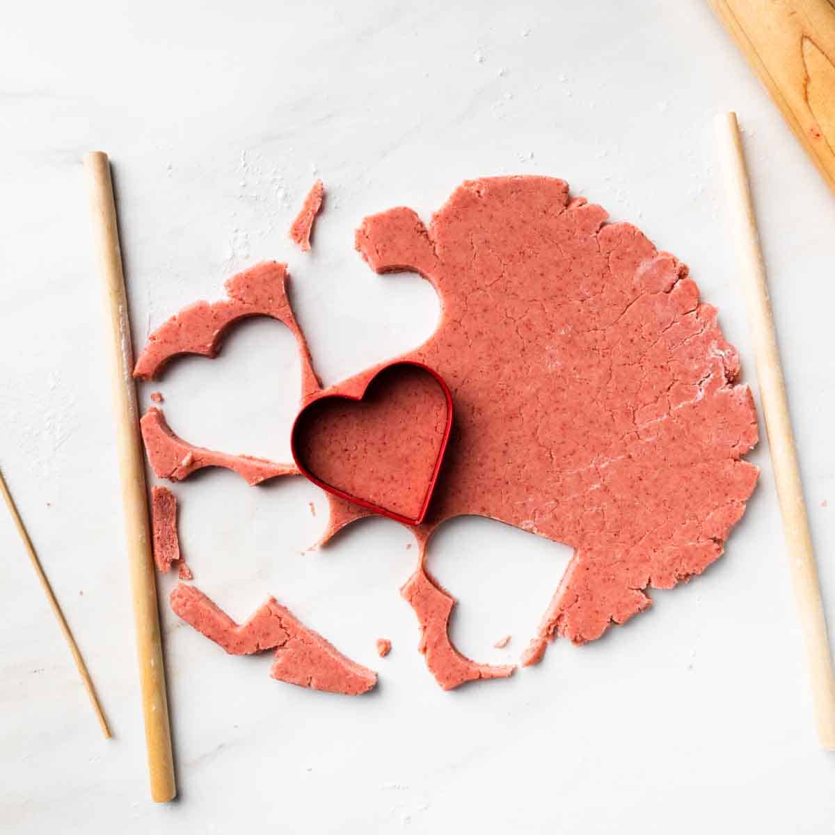 Rolled cookie dough with heart shaped cutouts and a red heart cookie cutter.