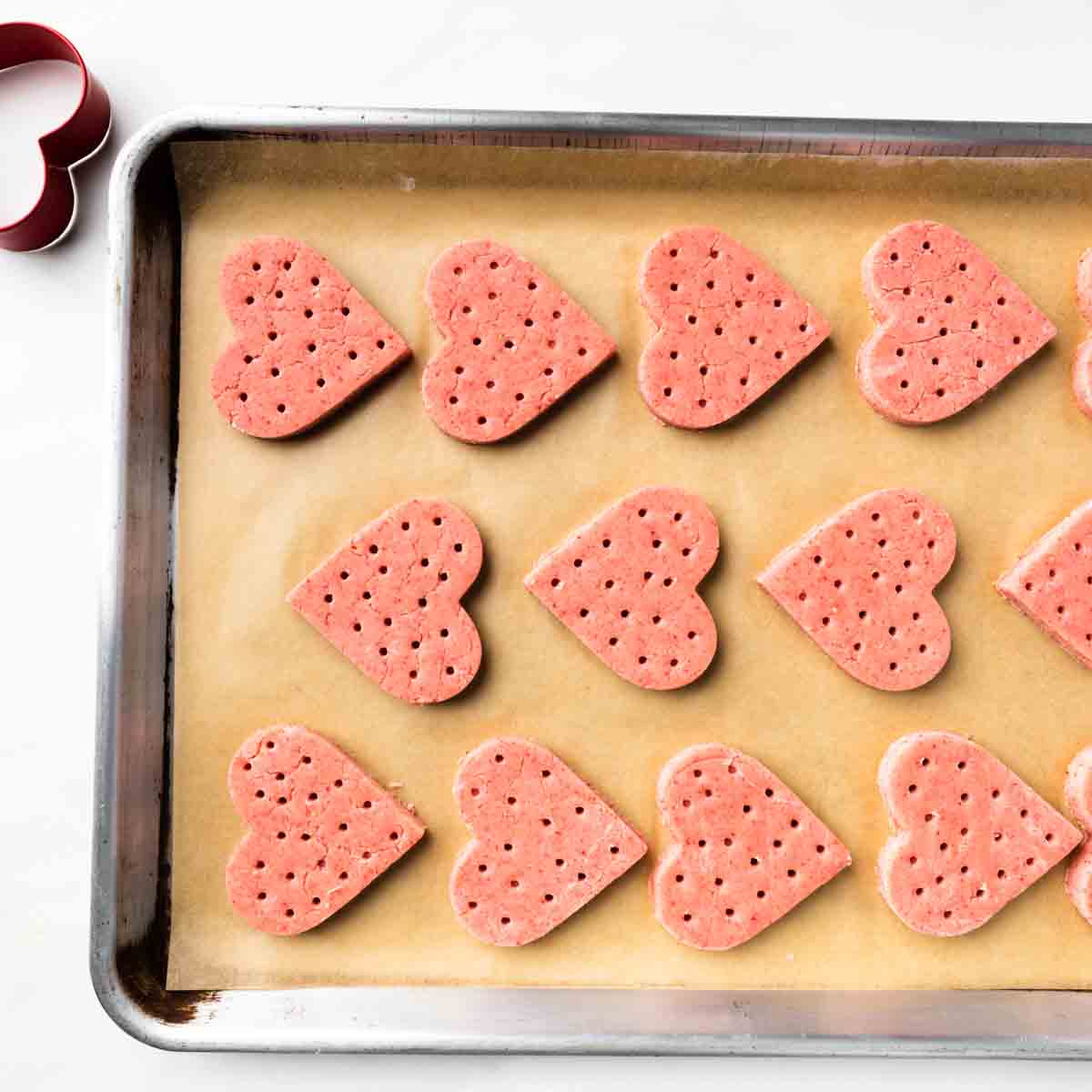 A parchment lined sheet tray of unbaked strawberry shortbread cookies.
