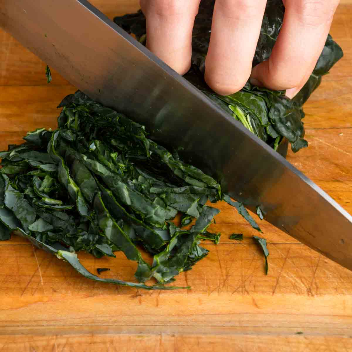 Thinly shaving the rolled kale leaves with a sharp knife.
