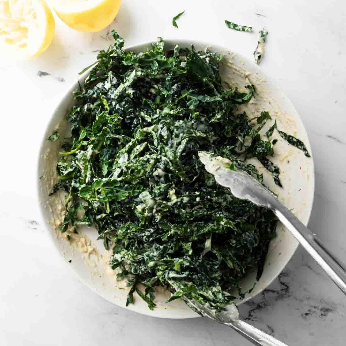Tossing the shaved kale in the dressing with tongs.