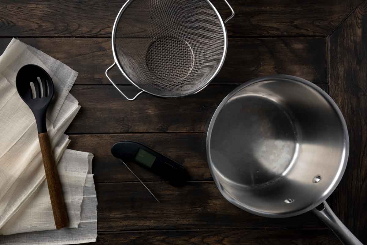 A stainless steel pot, a metal colander, an instant read thermometer, cheesecloth and a slotted spoon. 