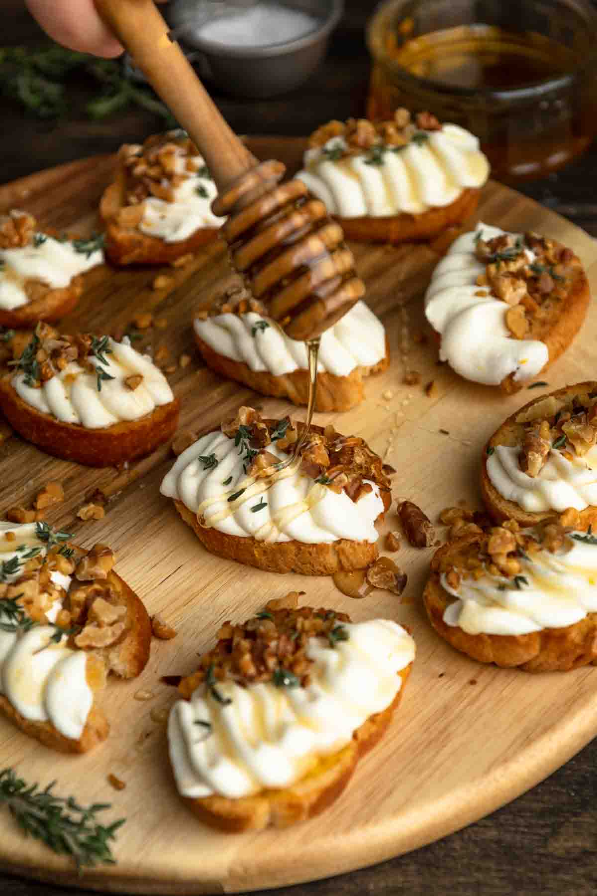 Drizzling honey over a board of whipped ricotta crostini appetizers. 