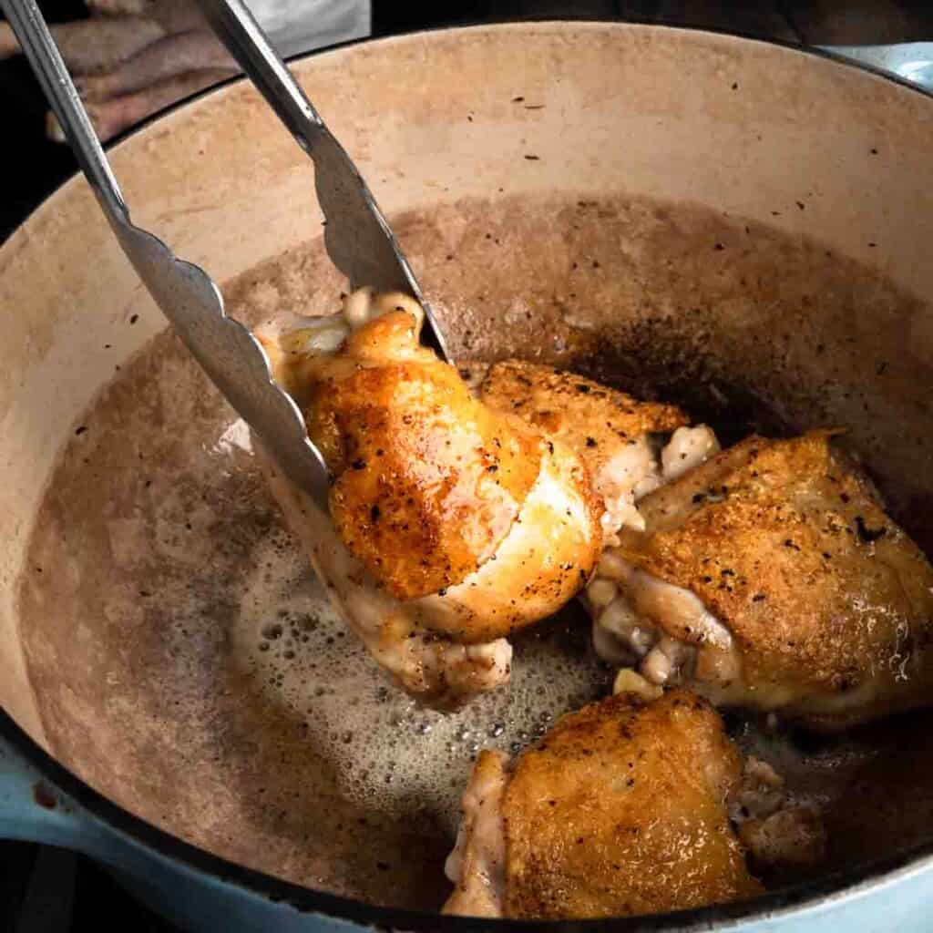 Lifting golden brown chicken thighs out of a Dutch oven.