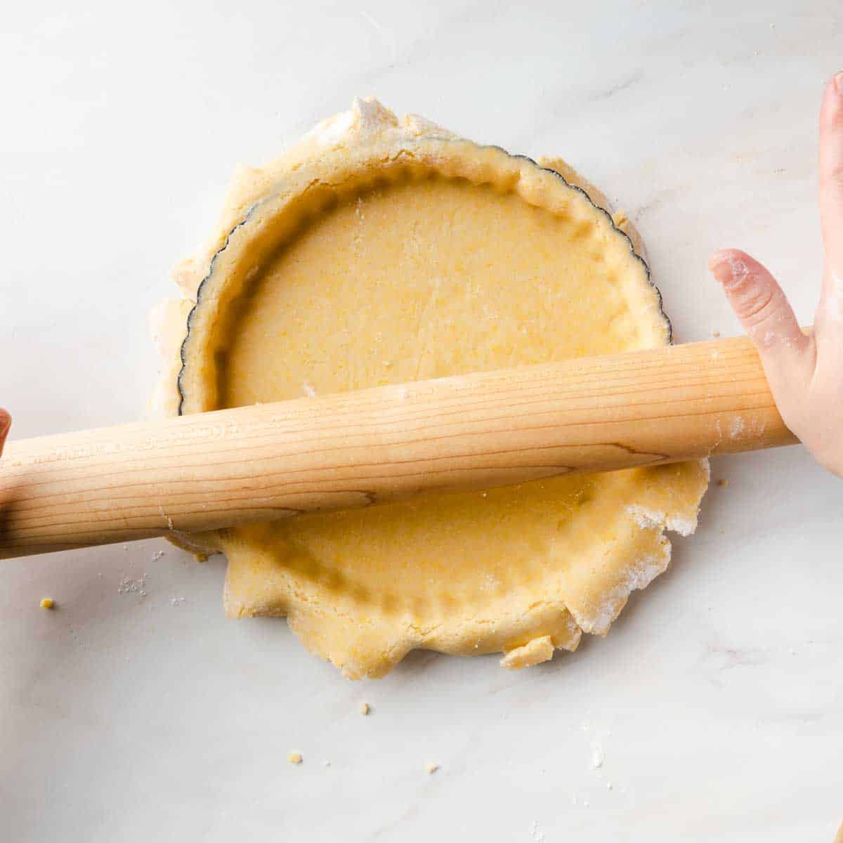 Trimming the edges of the dough in the pie plate with a rolling pin.