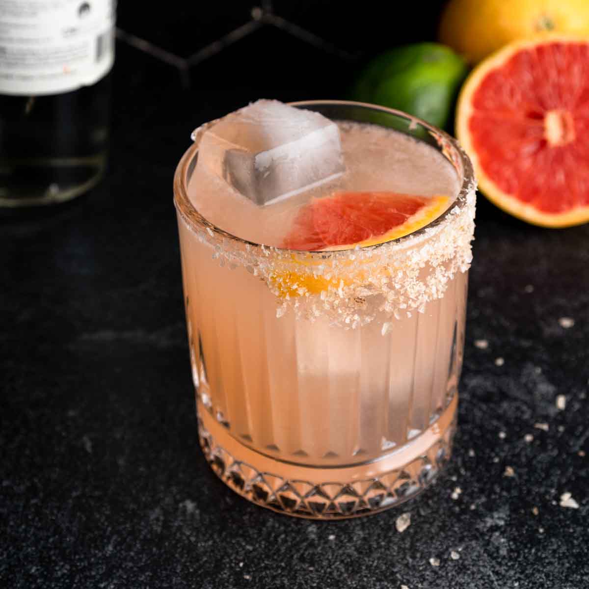 An icy mezcal cocktail in a glass rimmed with smoked salt next to a fresh grapefruit.